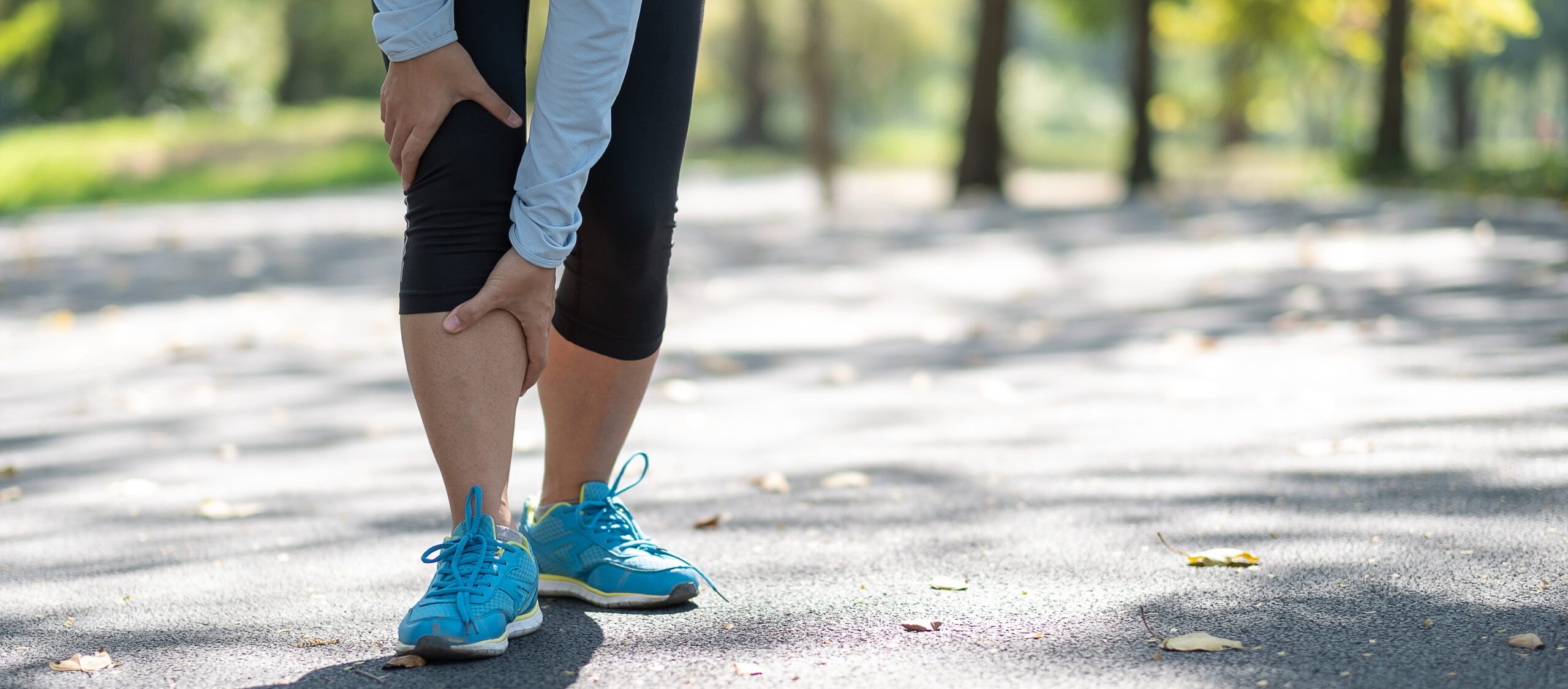 Young fitness woman holding his sports leg injury, muscle painful during training. Asian runner having calf ache and problem after running and exercise outside in summer